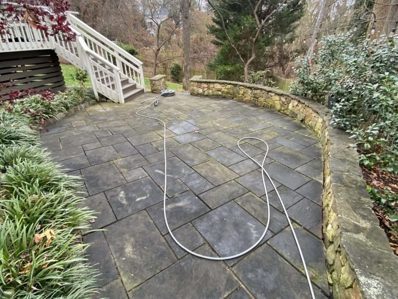 exterior paver patio and stone retaining wall covered in algae and growth before being power washed by alpha exterior cleaning